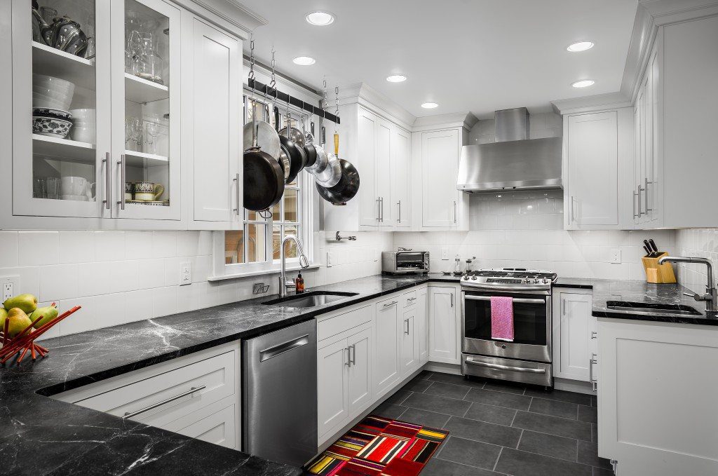 A traditional kitchen design with white cabinets, dark granite counter-tops, and stainless-steel appliances. Baker's rack over window.