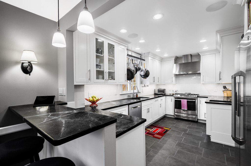 A modern kitchen design with white cabinets, dark granite counter-tops, and stainless steal appliances
