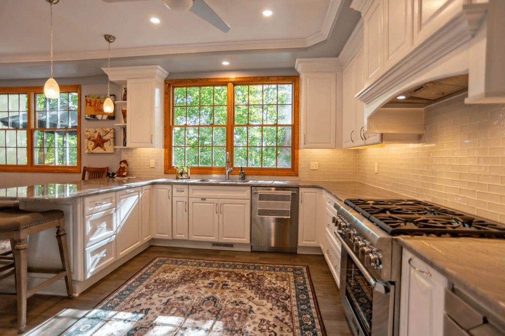 White kitchen in Ardmore, PA featuring an antique rug and a window over the sink framed in natural wood